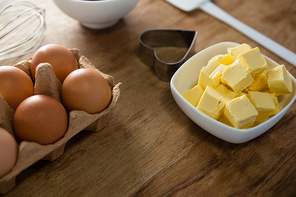 Close-up of eggs, butter cubes, whisk and cookie cutter on a wooden table