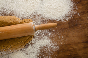 Over head view of flattening dough with a rolling pin with sprinkled over flour on a wooden table