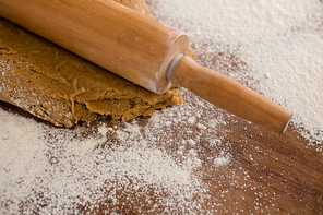 Close-up of view of flattening dough with a rolling pin with sprinkled over flour on a wooden table