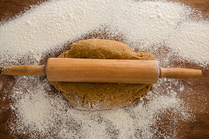 Over head view of flattening dough with a rolling pin with sprinkled over flour on a wooden table