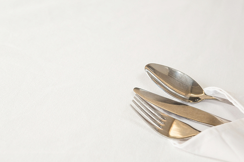 Fork, butter knife and spoon in napkin on white background
