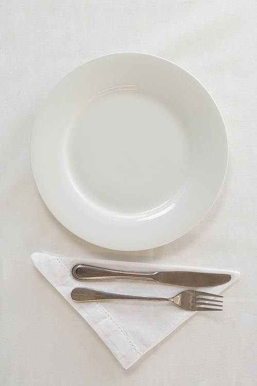 Overhead view of empty plate with fork, butter knife and napkin