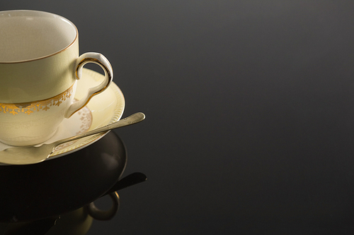 Close-up of empty cup with saucer and spoon on black background