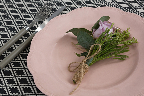 Close-up of fork and butter knife with flower and plate arranged on table cloth