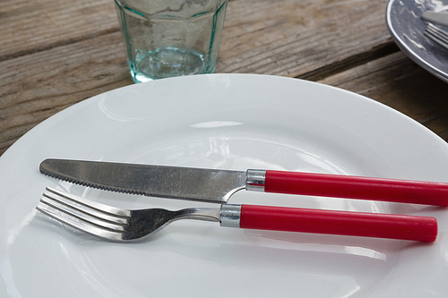 Close-up of plate with fork, butter knife and glass on wooden table