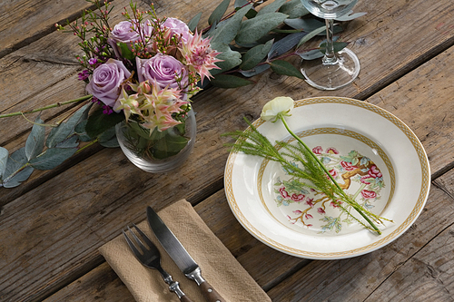 Close-up of fork and butter knife with plate and flower arranged on wooden table