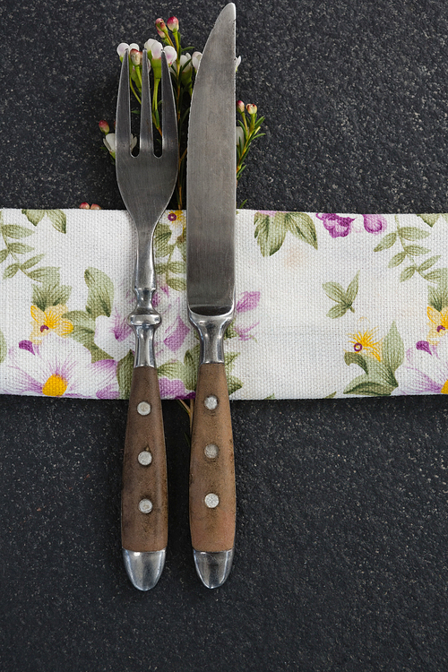 Close-up of fork and butter knife with flower and table cloth on black background