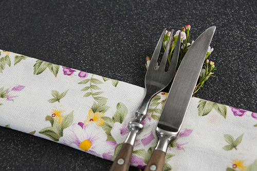 Close-up of fork and butter knife with flower and table cloth on black background
