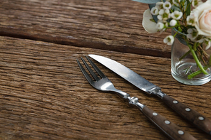 Close-up of fork and butter knife with rose flower n wooden table