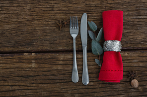 Overhead view of fork and butter knife with ingredients, leaf and napkin on wooden table