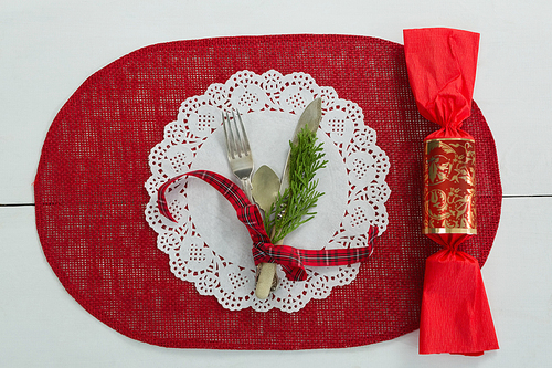 Overhead view of cutlery with fern tied up with ribbon and chocolate on a placemat