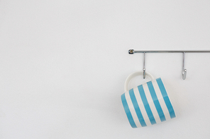 Striped mug hanging on hook against white wall