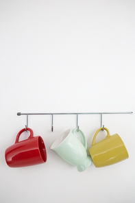 Colorful mugs hanging on hook against white wall