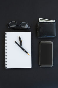 Overhead of spectacles, organizer, pen, mobile phone and wallet on background