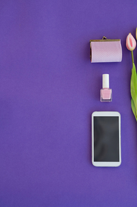 Overhead of tulips, purse, nail polish and mobile phone arranged on purple background