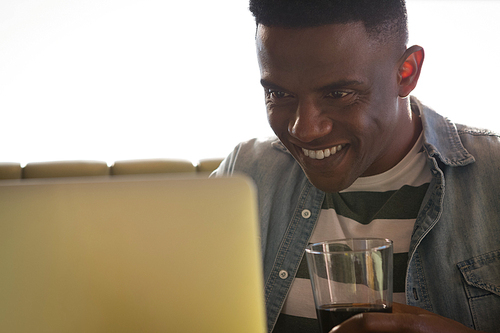 Close-up of happy young man holding glass while working on laptop