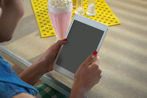 Close-up of woman using tablet while having milkshake in the restaurant