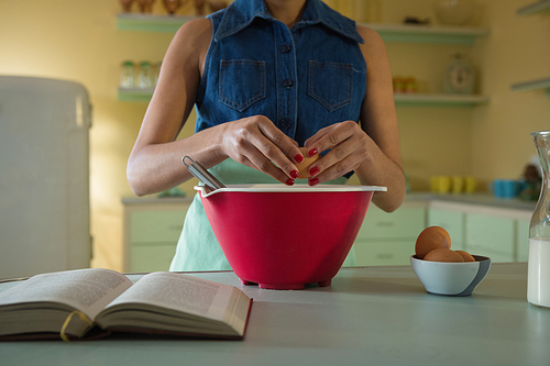 Young woman breaking an egg in to mixture bowl at kitchen