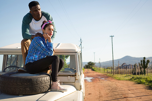 Young couple sitting on car bonnet at countryside