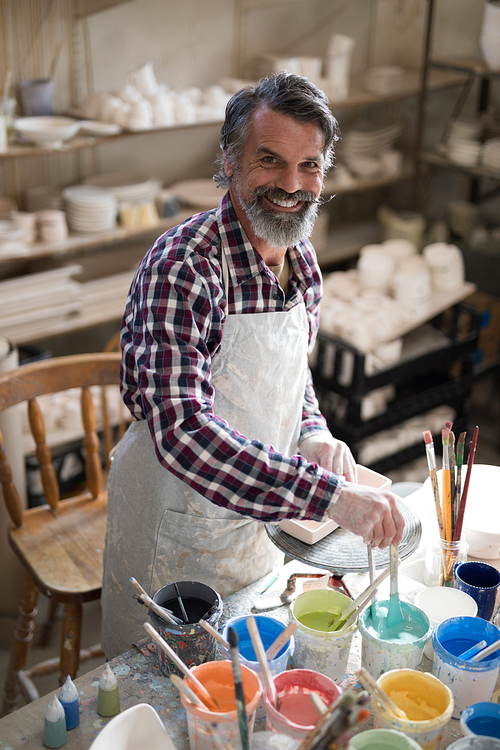 Portrait of smiling male potter holding color tube in pottery shop