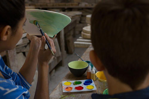 Female potter assisting her son in painting a bowl at pottery shop