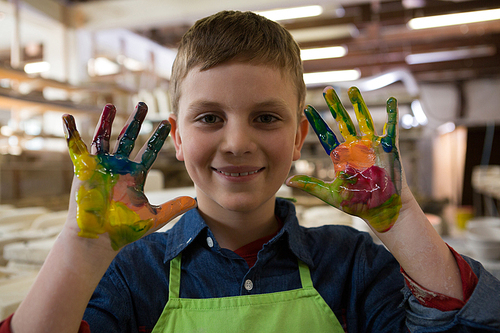 Boy showing colorful paint on his hands at pottery shop