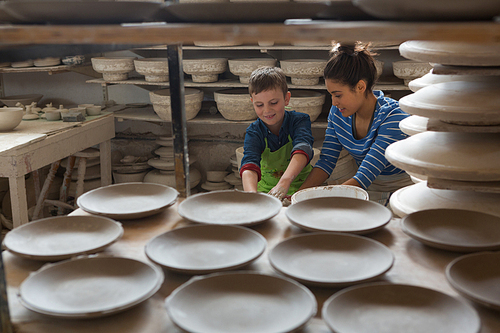 Female potter assisting a boy in pottery workshop