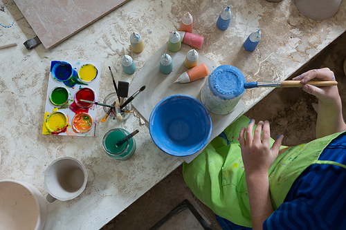 Mid-section of boy painting a bowl in pottery shop