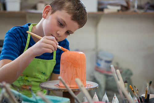 Attentive boy painting a bowl in pottery shop