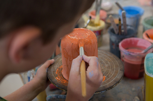Close-up of boy painting a bowl in pottery shop