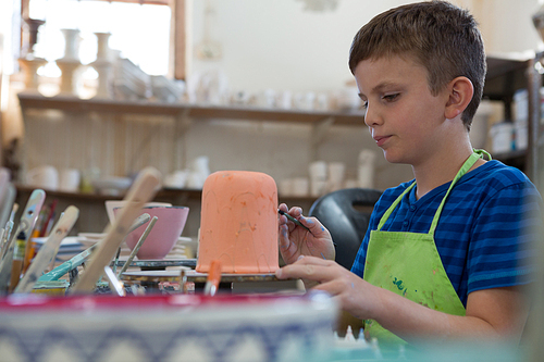 Attentive boy painting a bowl in pottery shop