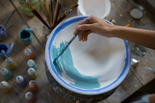 Female potter hand painting a bowl in pottery shop