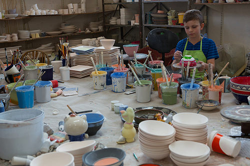 Attentive boy painting a bowl in pottery shop