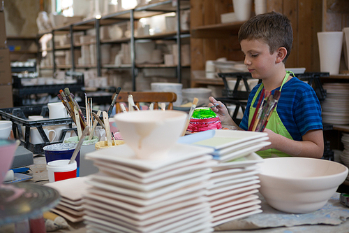 Attentive boy painting a bowl in pottery shop
