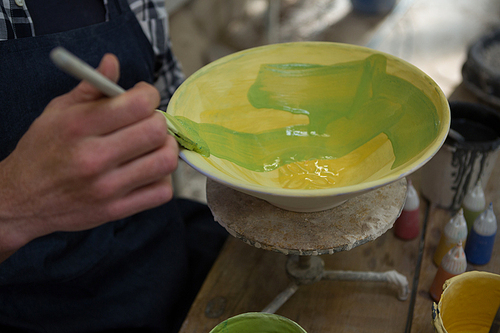 Mid-section of male potters hand painting a bowl in pottery workshop