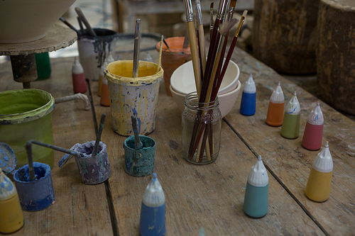 Close-up of watercolor cans and paintbrush in pottery workshop