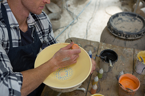 Mid-section of male potters painting a bowl in pottery workshop