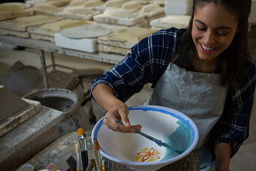 Female potter painting a bowl in pottery workshop