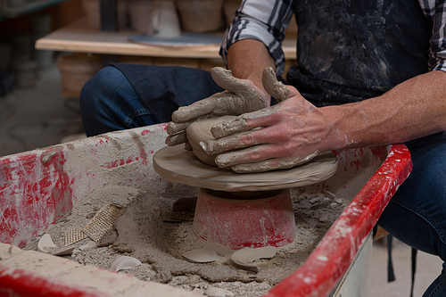 Mid-section of male potter making a pot in pottery workshop