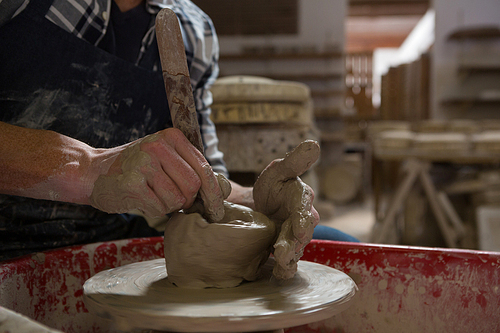 Mid-section of male potter making a pot in pottery workshop