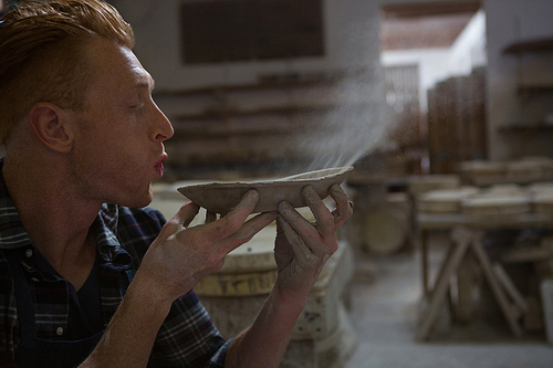 Male potter blowing dust from a bowl in pottery workshop