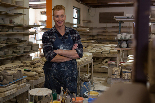 Portrait of male potter standing with arms crossed in pottery workshop