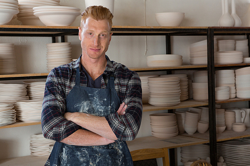 Portrait of male potter standing with arms crossed in pottery workshop