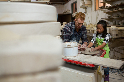 Male potter assisting his daughter in making a pot in pottery workshop