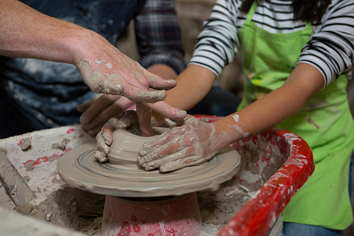 Male potter assisting his daughter in making a pot in pottery workshop
