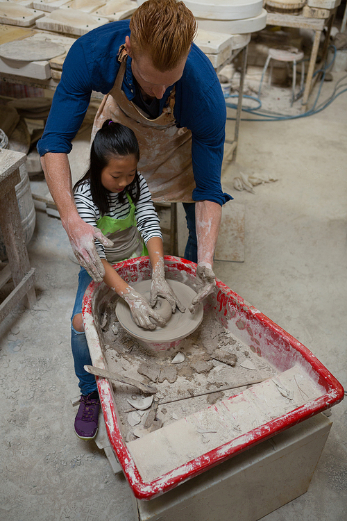 Male potter assisting girl in molding a clay at workshop