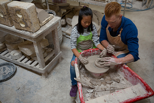 Male potter assisting girl in molding a clay at workshop