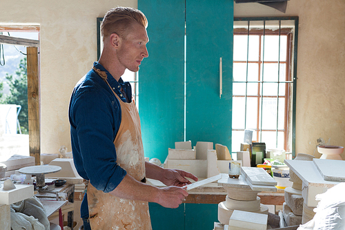 Thoughtful male potter using digital tablet in pottery workshop