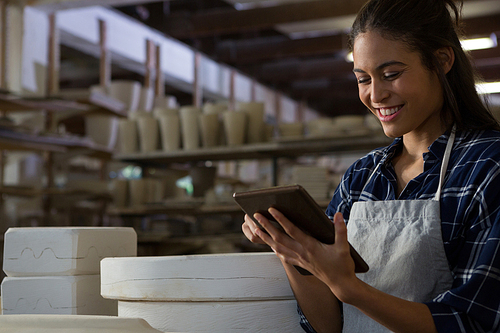 Happy female potter using digital tablet in pottery workshop