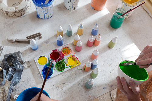 Hands of male potter and girl painting bowl in pottery workshop